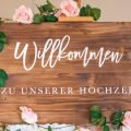 Wooden welcome sign adorned with pink roses for a wedding celebration.