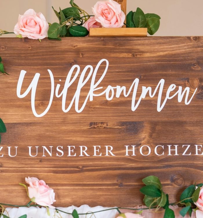 Wooden welcome sign adorned with pink roses for a wedding celebration.
